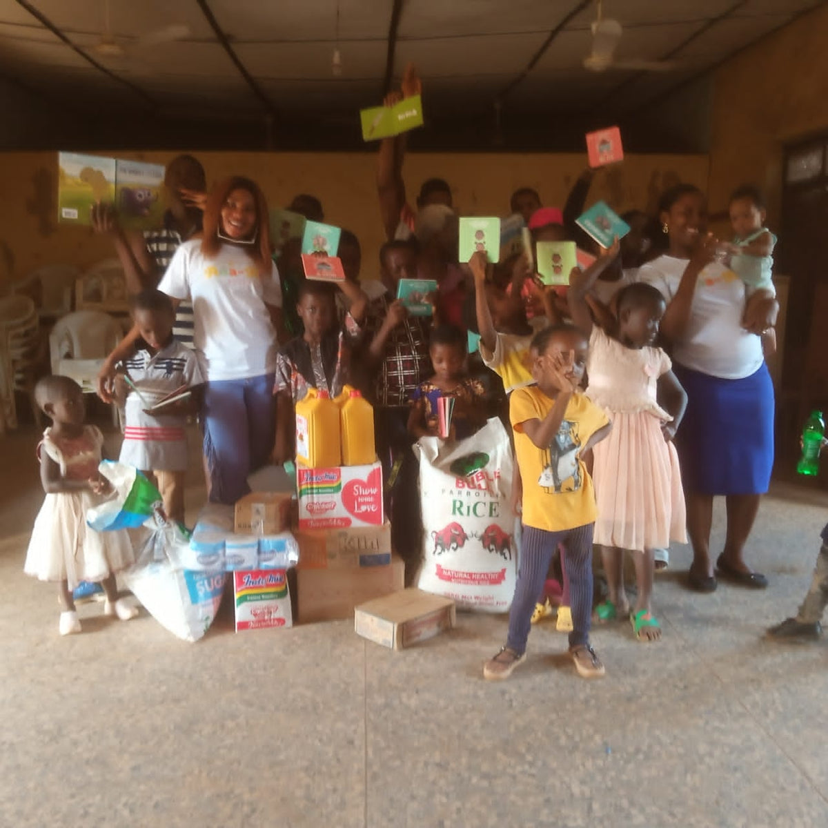 Children holding up KOLI & OLUM books beside donated supplies